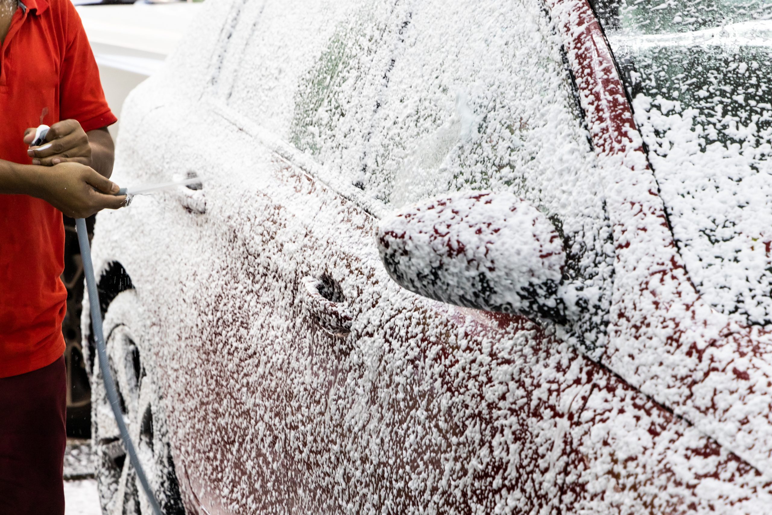 Detergent soap foam known as snow wash sprayed onto car at garage before washing